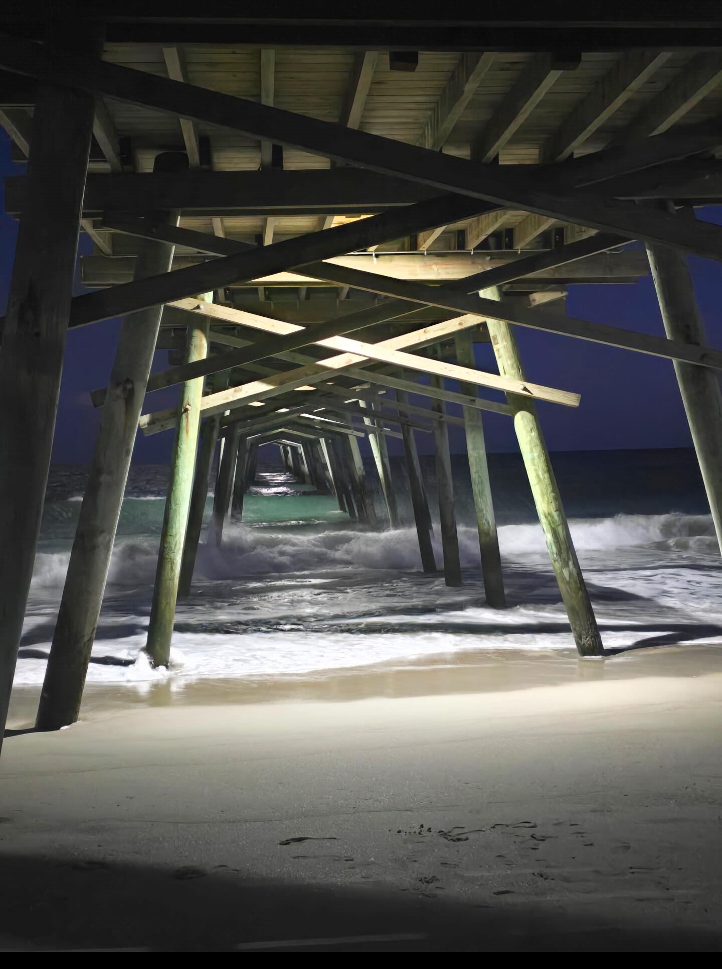 Night view beneath the Emerald Isle Fishing Pier with waves rolling in along the beach.